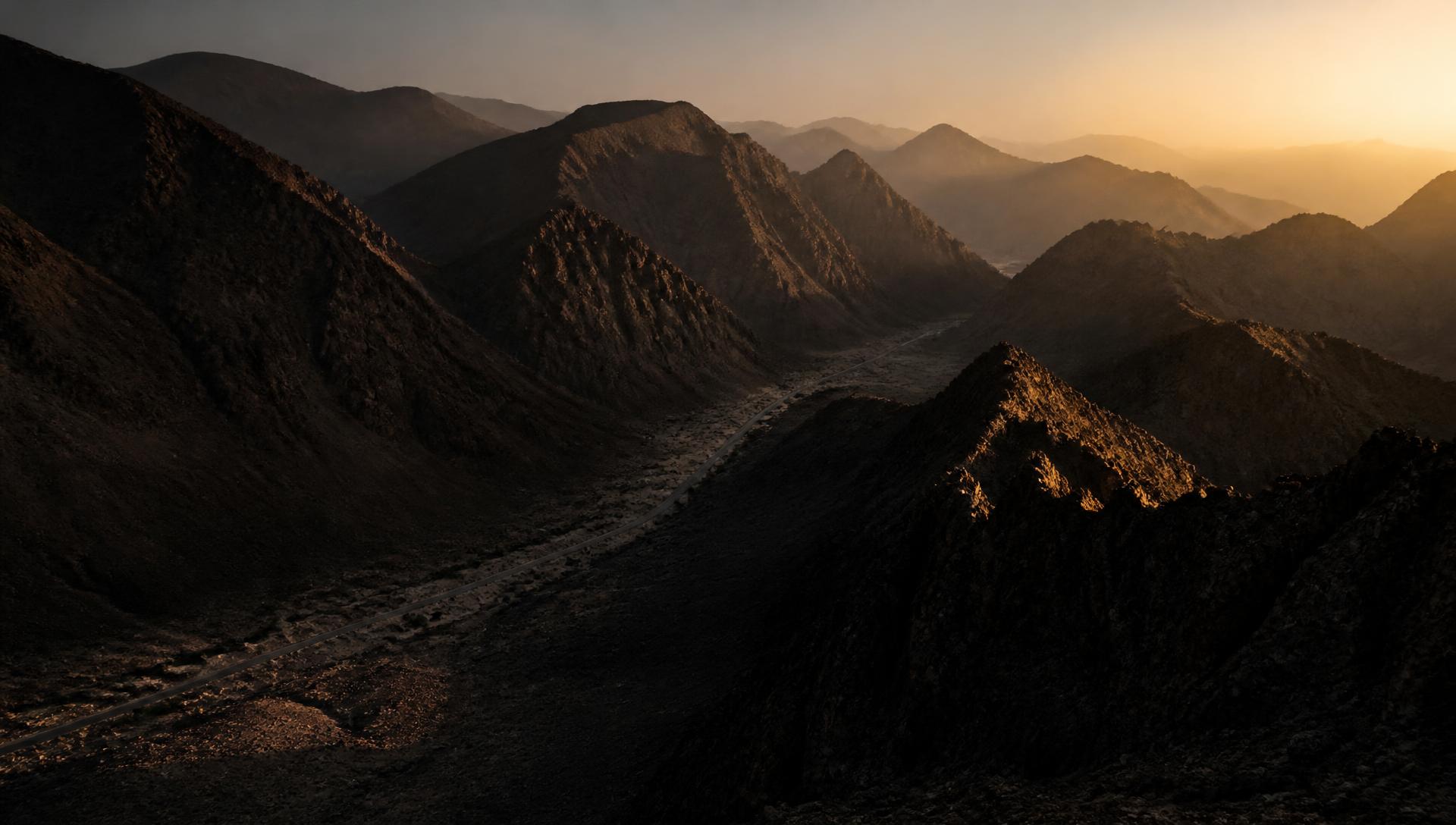 First light across the Hajar mountains of Oman, a thin road running through the valley